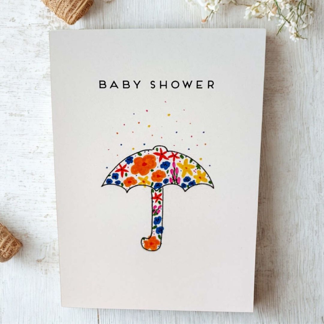 Baby shower card with floral umbrella design on a wooden surface_Just Makers