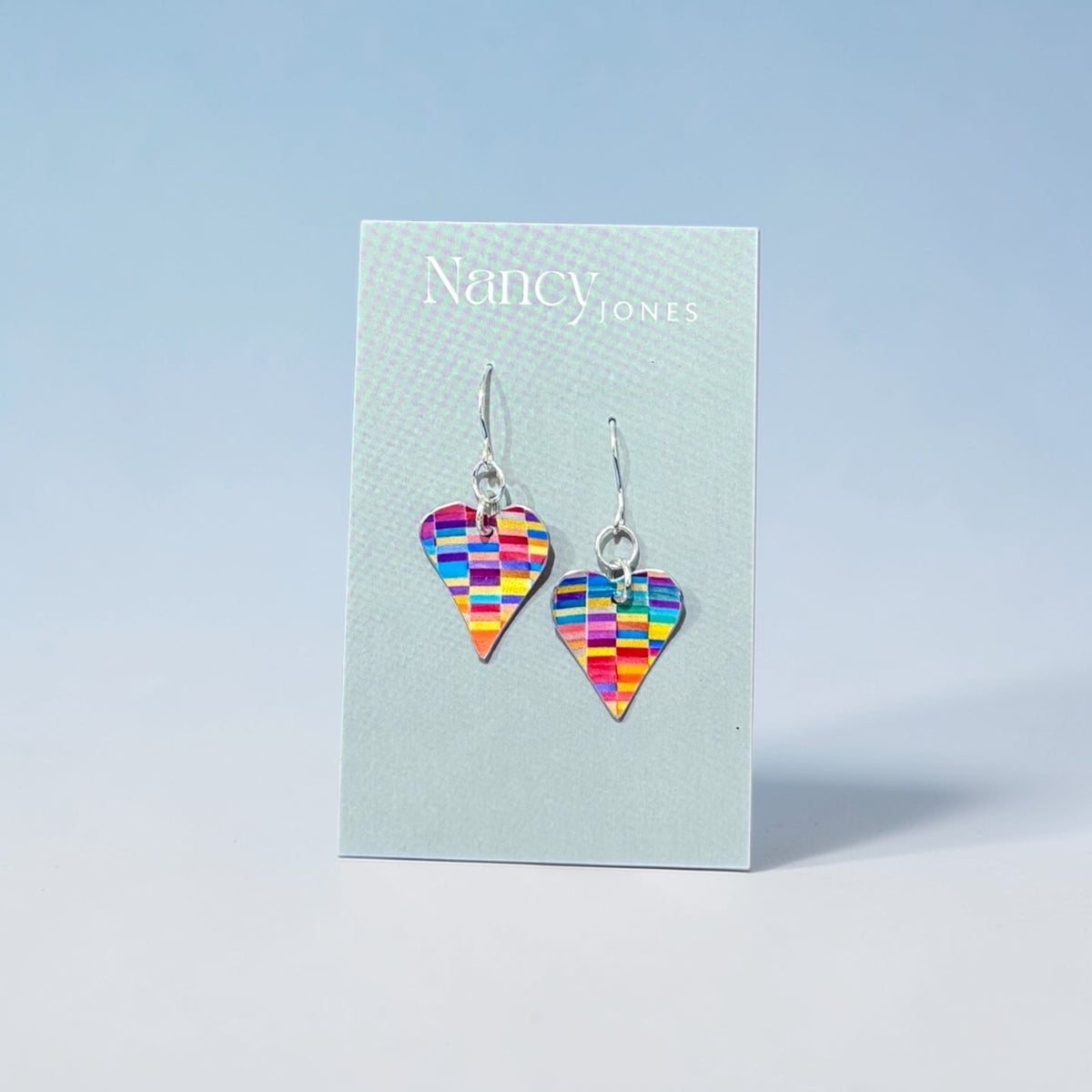 Colorful heart-shaped earrings on a Nancy Jones card against a light blue background