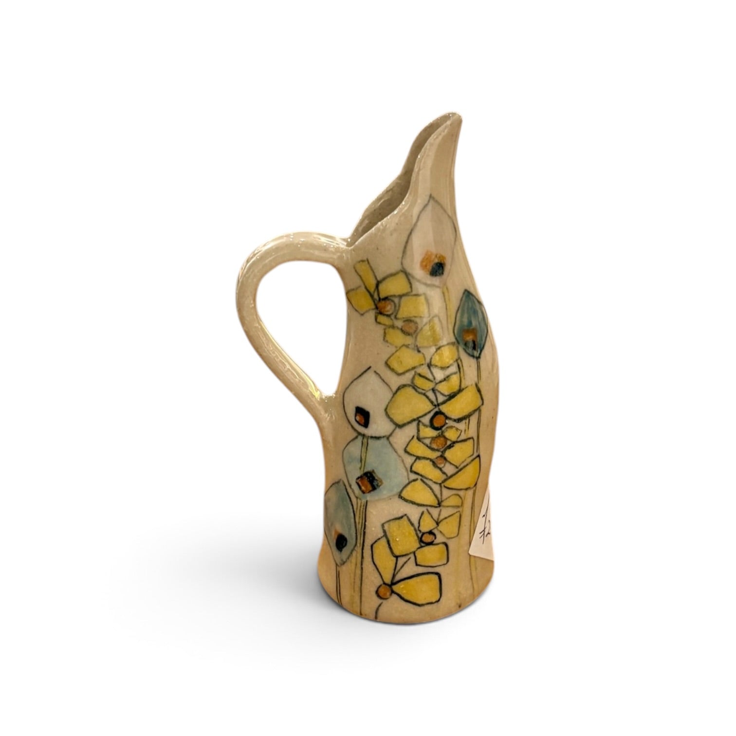 A hand-painted ceramic pitcher with a curved handle, featuring a light beige background decorated with yellow flowers, green leaves, and small orange accents, set against a plain white background.