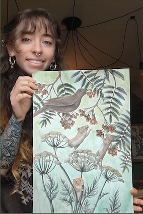 A woman holding up a square art print featuring a nature illustration of a bird perched on branches with leaves and berries, set against a light mint green background.