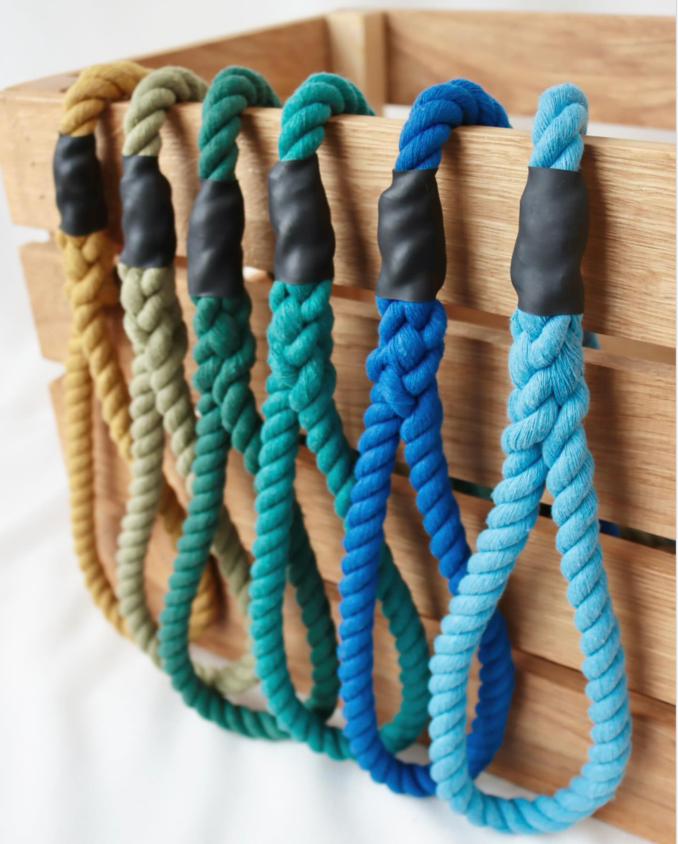 Five thick twisted rope handles in assorted colors hanging from a wooden crate. The rope ends are secured with black rubber or plastic collars.