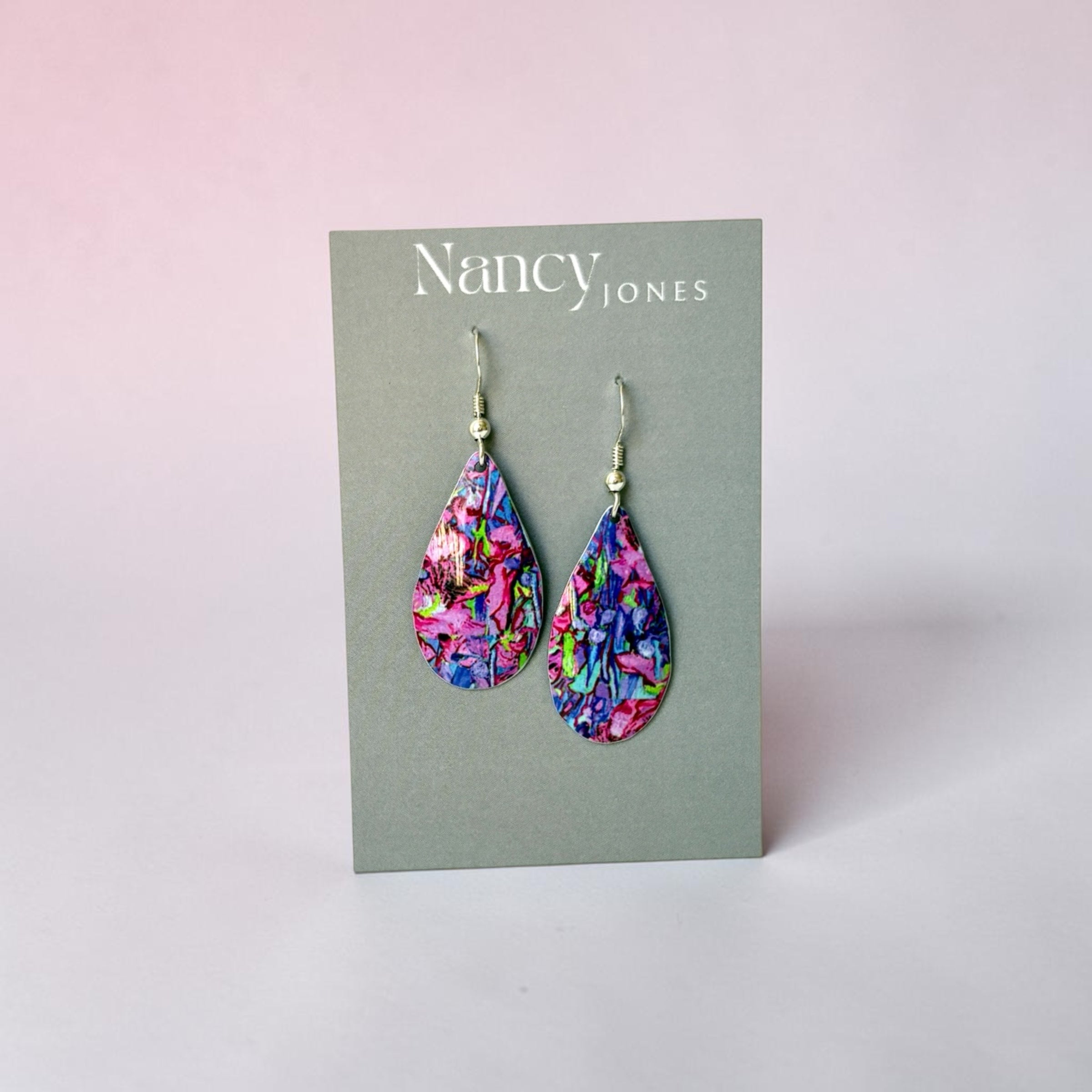Colorful teardrop earrings on a Nancy Jones card against a light pink background