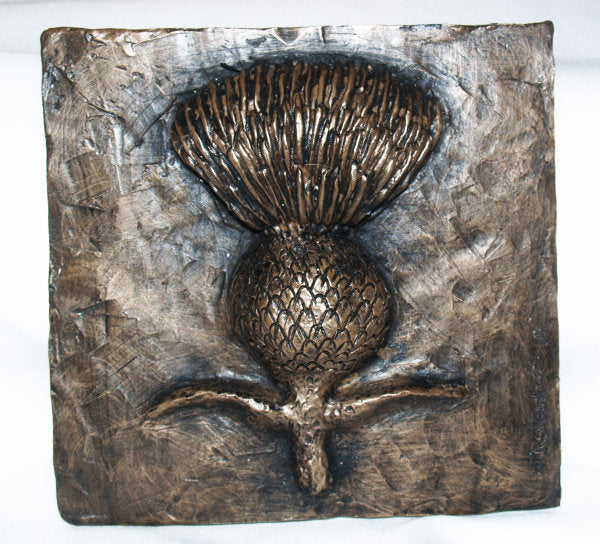 A square bronze wall plaque featuring a raised thistle design with textured metallic surfaces and a rustic finish, photographed against a plain white background.
