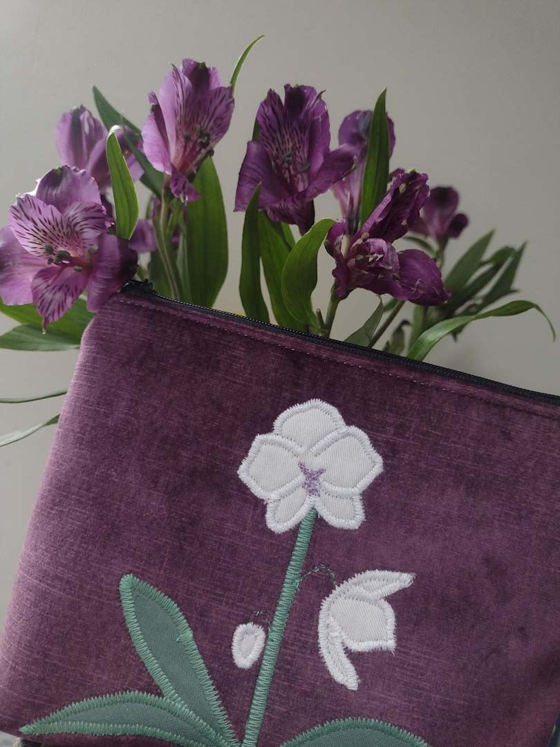 Purple pouch with floral embroidery next to purple flowers_Just Makers