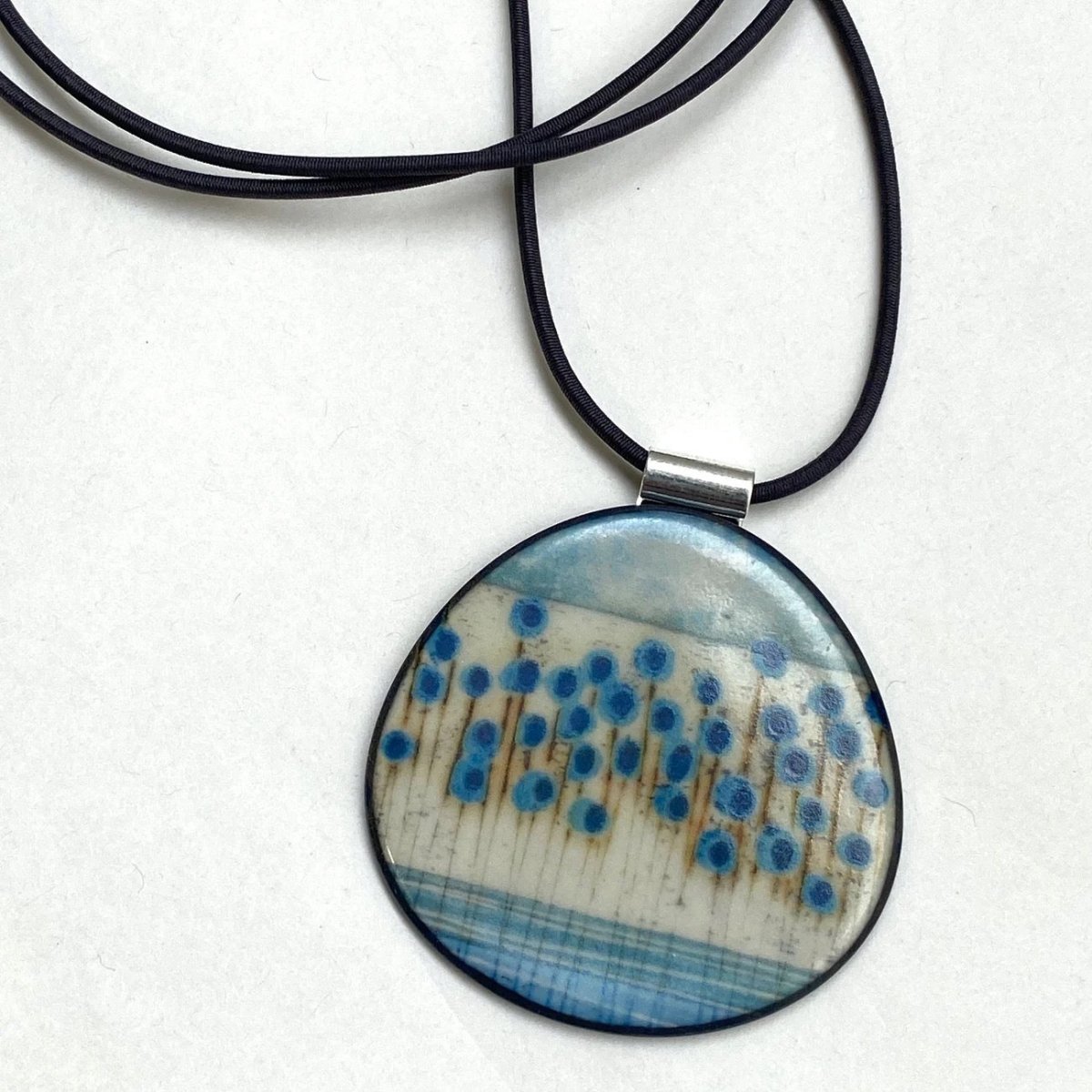 Round pendant with blue and brown pattern on a black cord against a white background