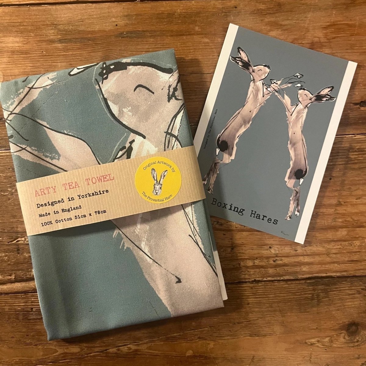 Tea towel with hares design and a card featuring hares on a wooden surface