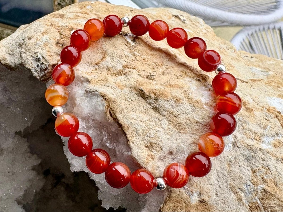 Red beaded bracelet with silver accents on a rock