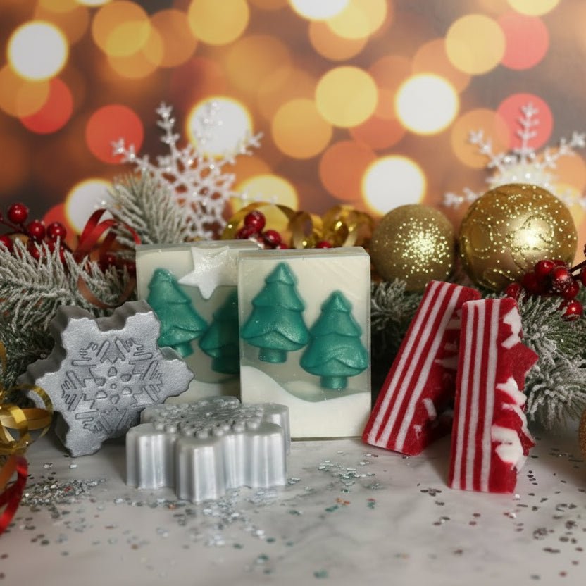 A set of handmade winter-themed soaps displayed on a white marble surface against a white background. The set includes a gray snowflake soap, a silver snowman soap, two green Christmas tree soaps in their clear packaging, and two red and white striped soaps resembling candy canes.
