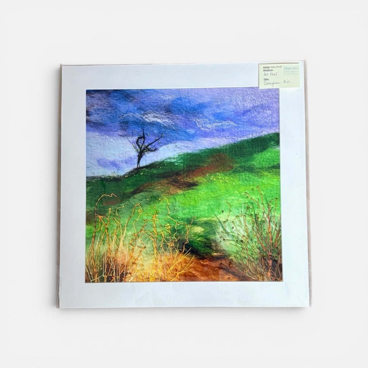 Framed painting of a landscape with a tree on a hillside.