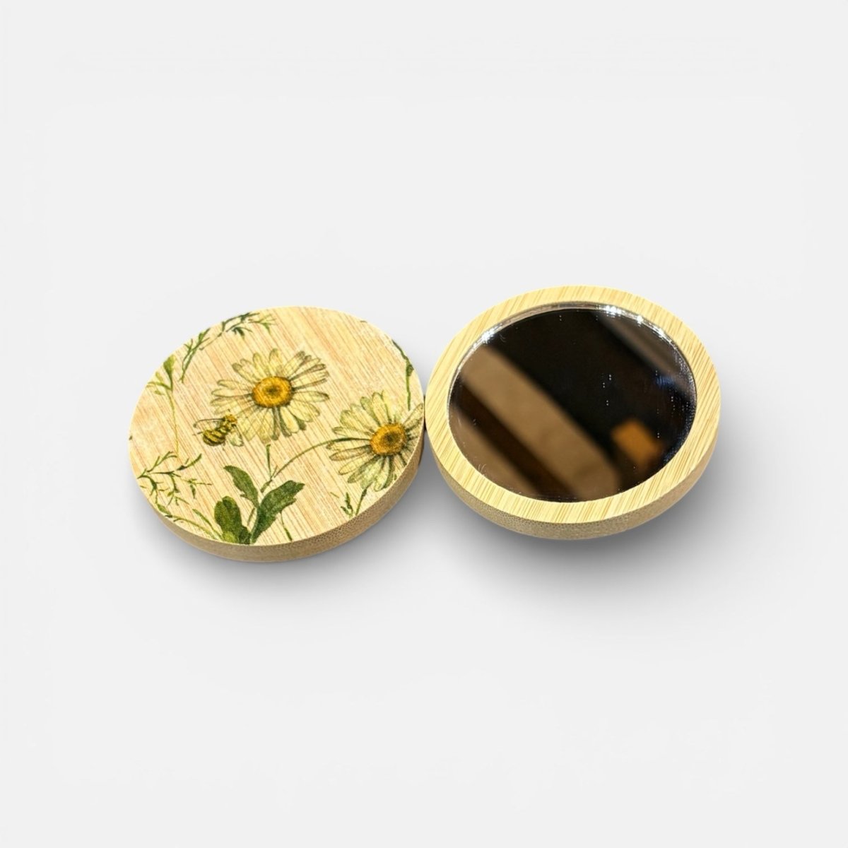 Round wooden compact mirror with floral design on one side and black interior on the other, on a white background.