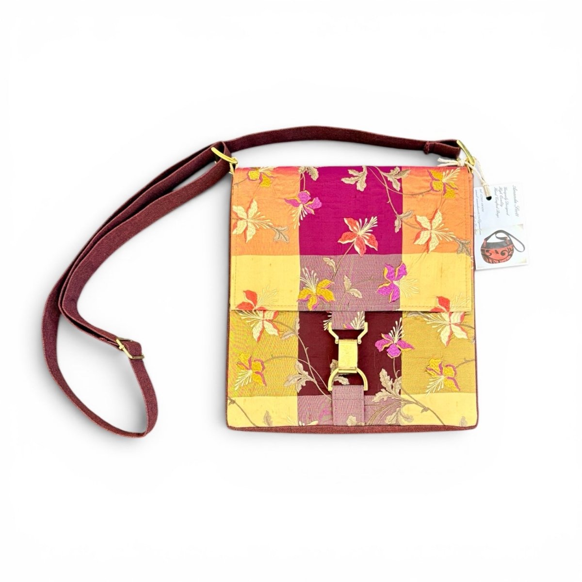 A square crossbody handbag with a multicolor patchwork floral pattern in shades of yellow, orange, pink, and purple, featuring a burgundy strap and gold-tone hardware, shown with its product tag on a white background.