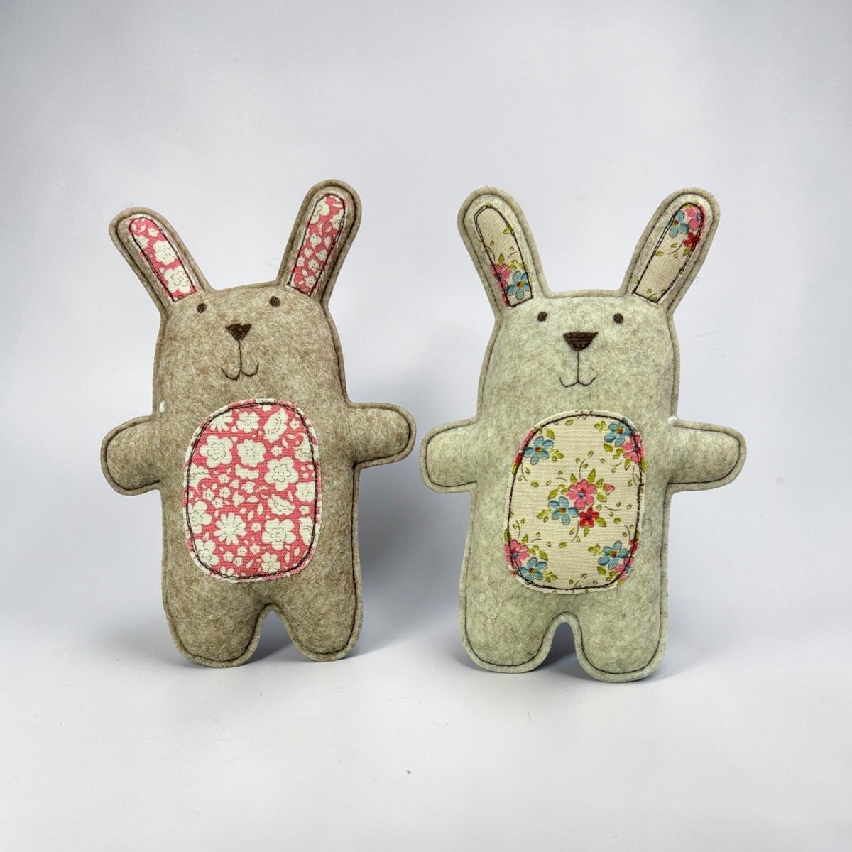 Two fabric bunnies with floral patterns on a white background