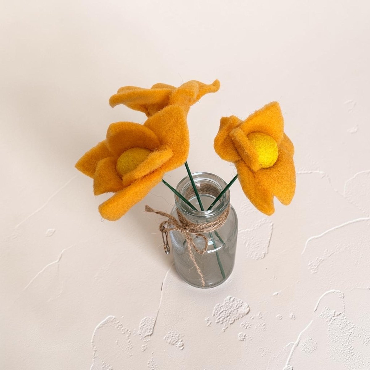 Yellow felt flowers in a small glass jar on a light background