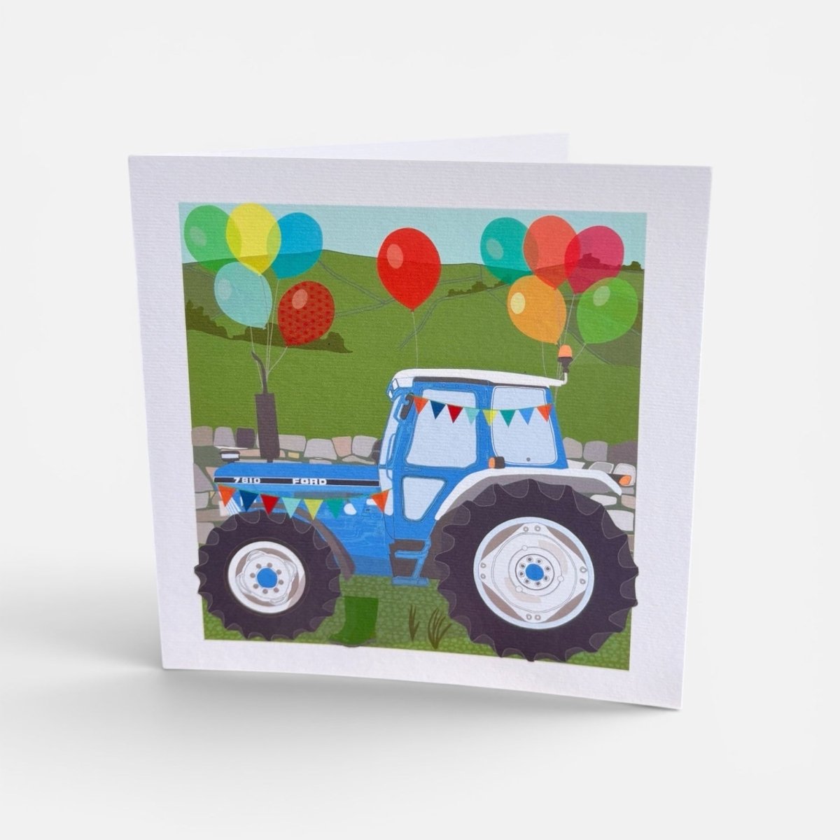Card with a blue tractor and colorful balloons on a white background
