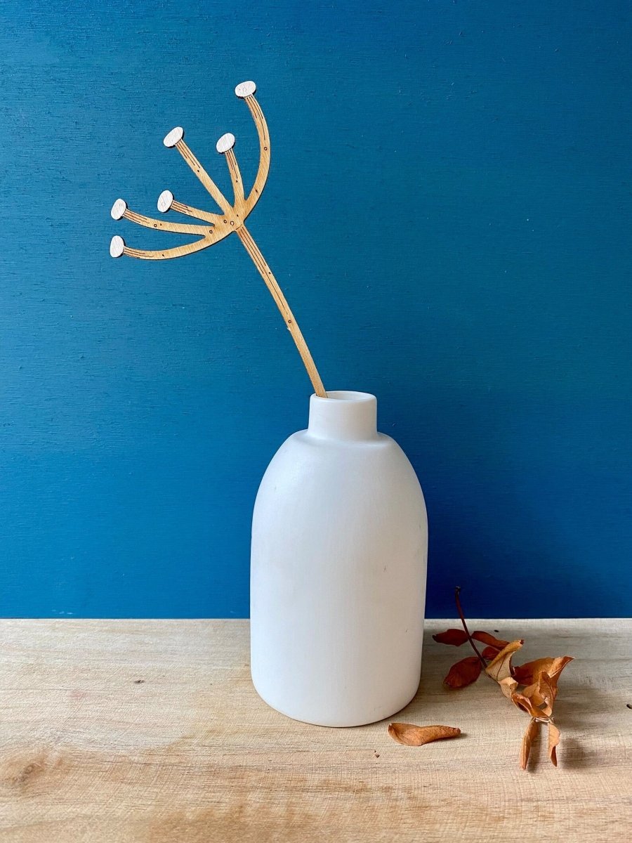 White vase with a dried plant against a blue wall on a wooden surface