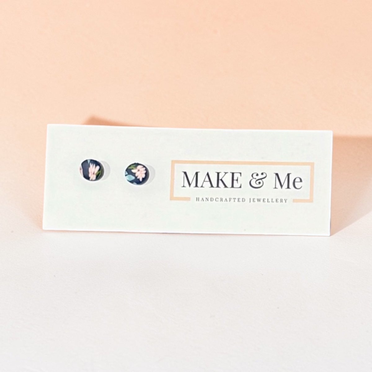 Make & Me earrings on a branded card with a pink background