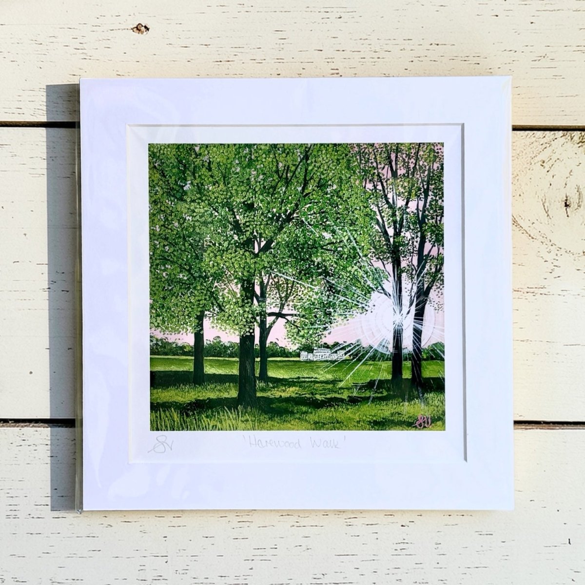 Framed artwork of a green landscape with trees on a wooden surface