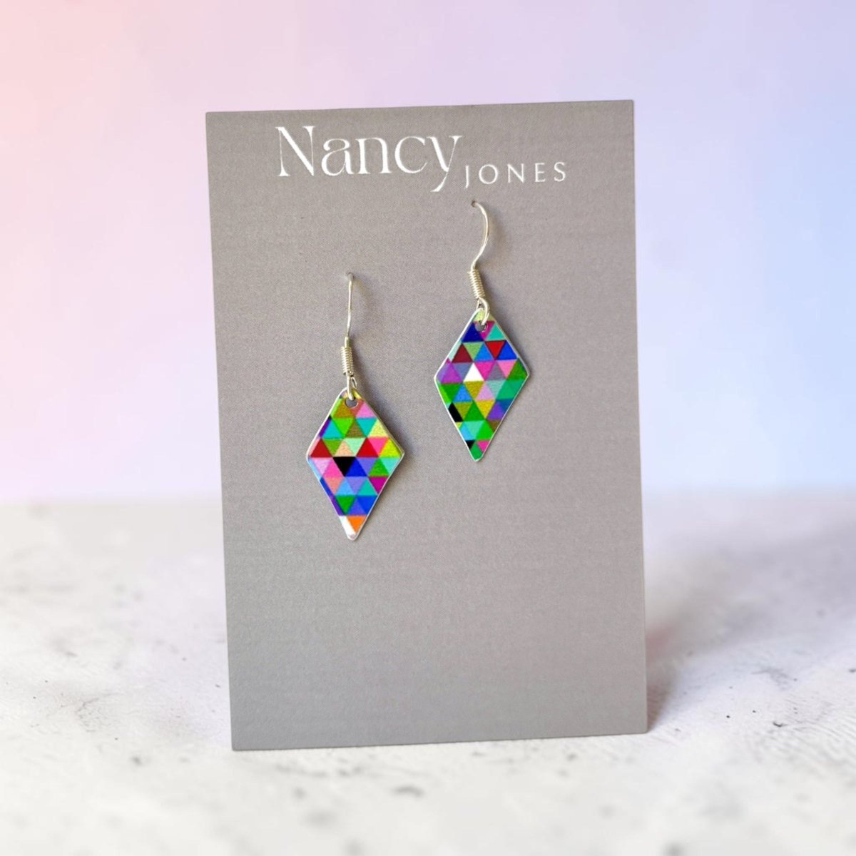 Colorful diamond-shaped earrings on a Nancy Jones card against a light background