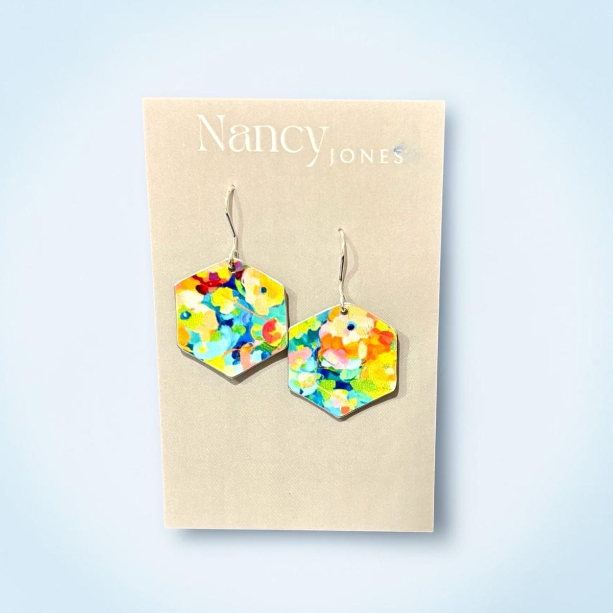 Colorful hexagonal earrings on a Nancy Jones card against a light blue background