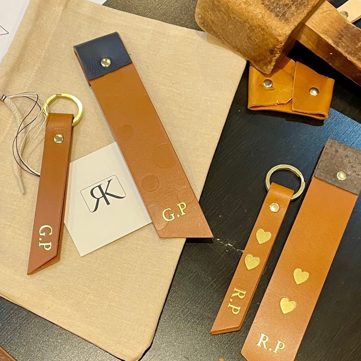 Collection of leather keychains and straps with initials on a wooden surface