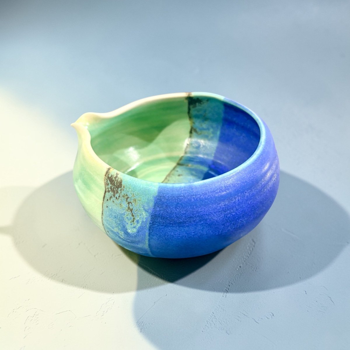 Ceramic bowl with green and blue glaze on a light gray background