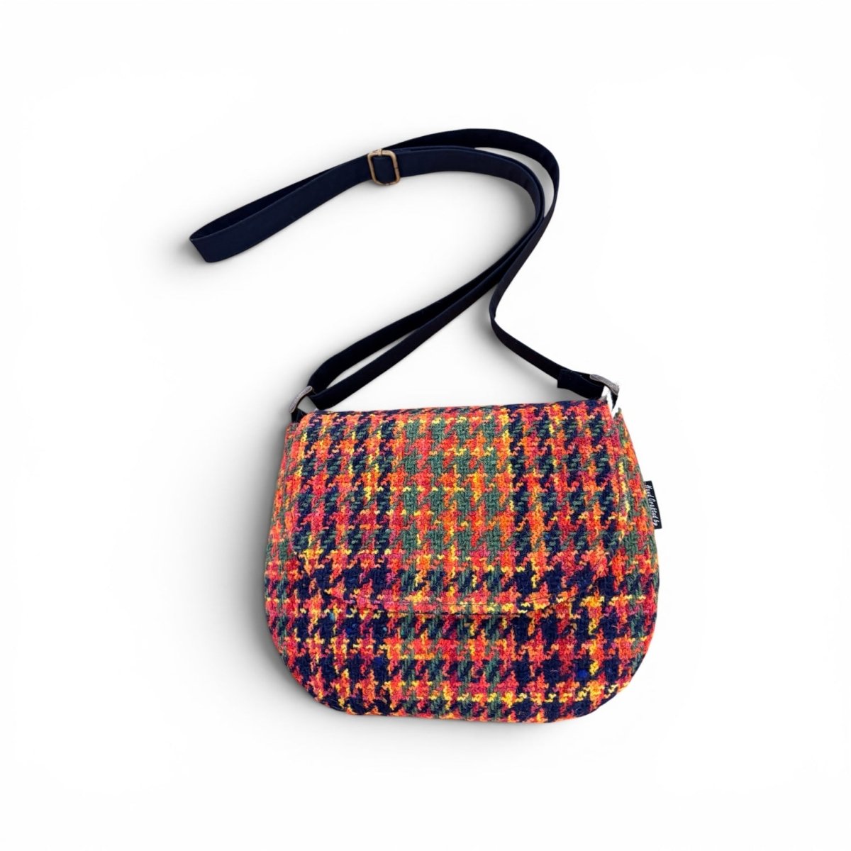 A small shoulder bag with a vibrant multicolor houndstooth pattern in red, orange, yellow, green, and blue, featuring a dark navy blue strap with gold-tone hardware, shown on a plain white background.