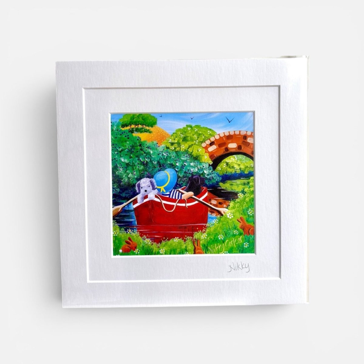 Framed artwork of two dogs in a red rowboat with a bridge and trees in the background.