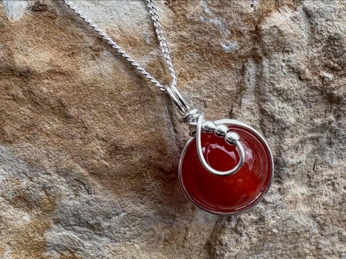 Silver necklace with a red pendant on a stone background