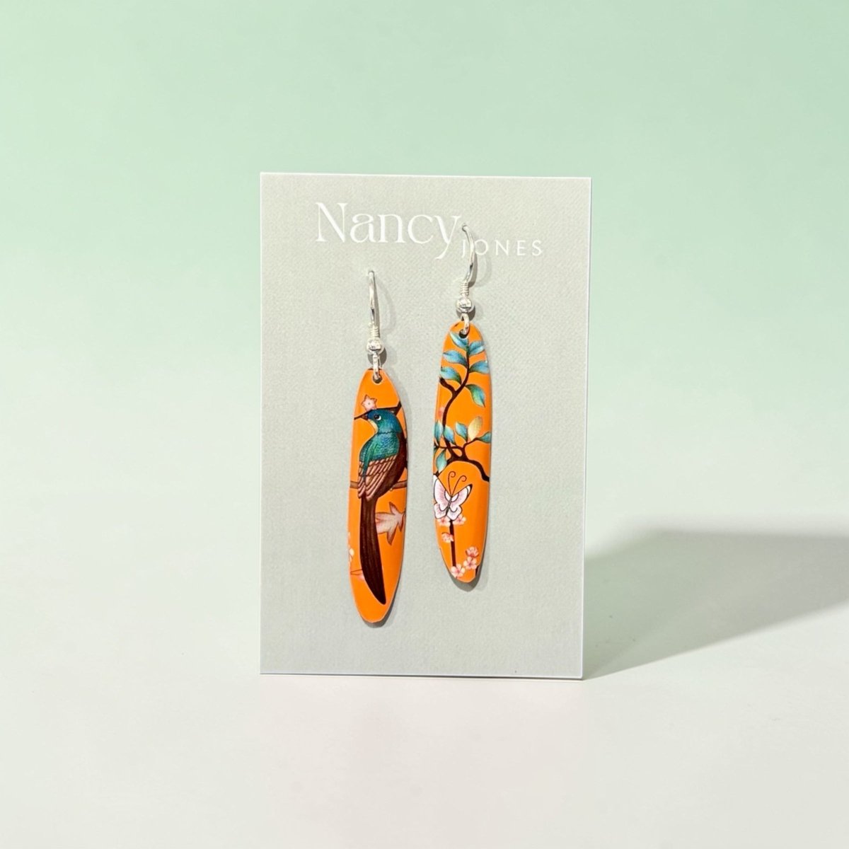 Orange earrings with floral design on a Nancy Jones card against a light green background