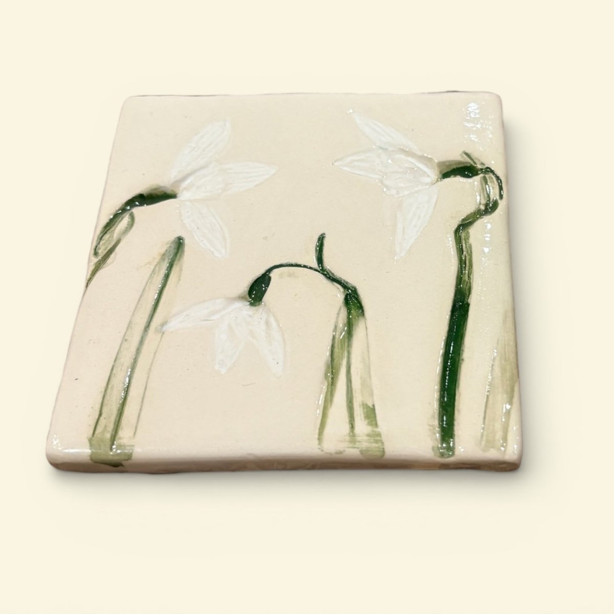 Square ceramic tile with snowdrop flowers on a beige background