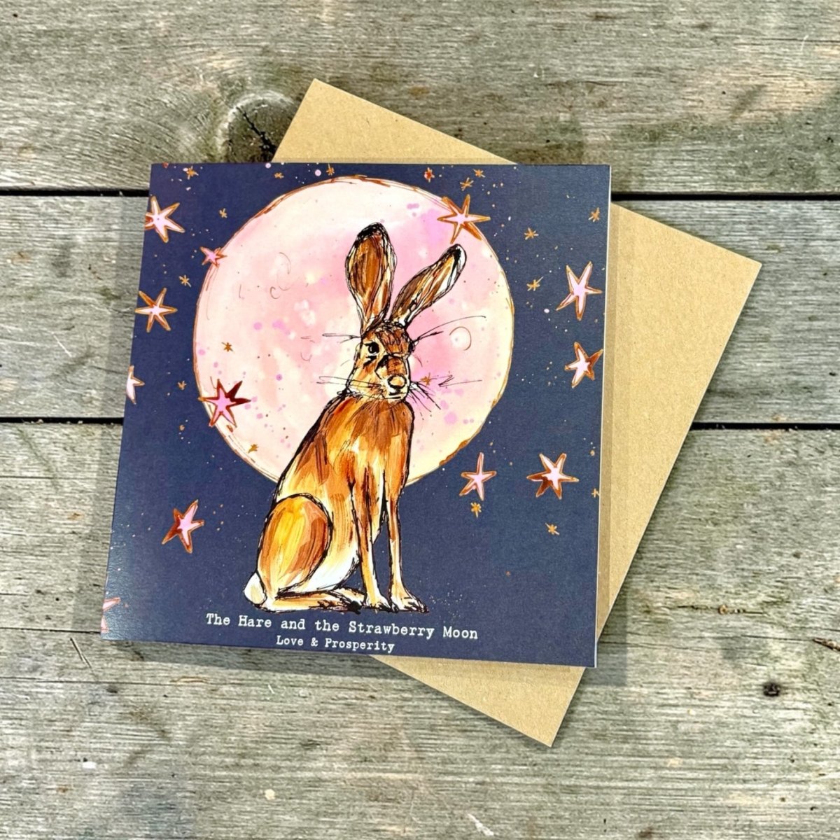 Card with a hare illustration and strawberry moon design on a wooden surface