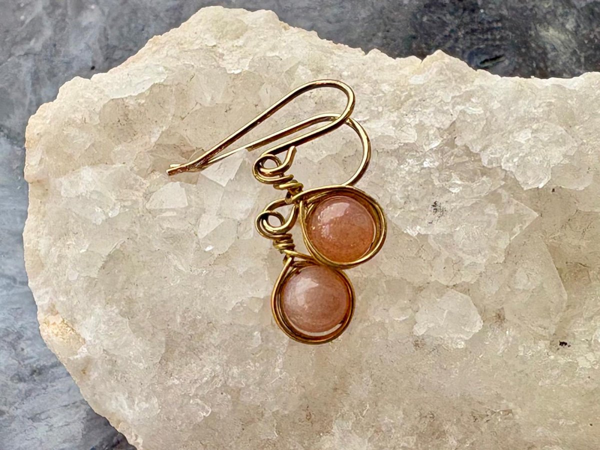 Gold earrings with peach-colored gemstones on a textured stone surface