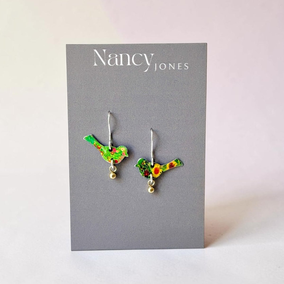 Bird-shaped earrings on a Nancy Jones card with a light pink background