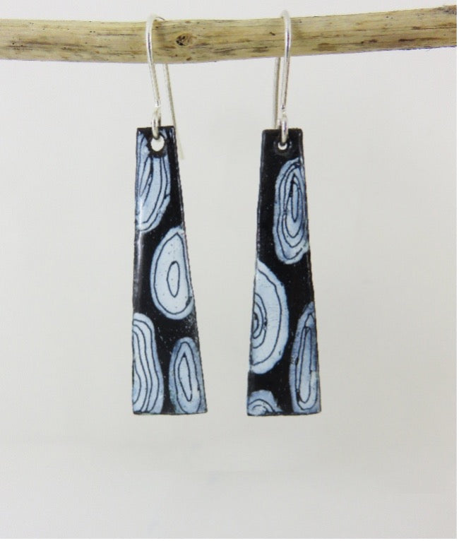 Black and white patterned earrings hanging from a branch on a light gray background