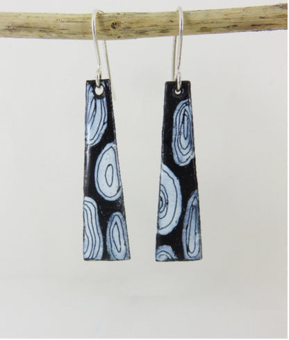 Black and white patterned earrings hanging from a branch on a light gray background