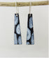 Black and white patterned earrings hanging from a branch on a light gray background