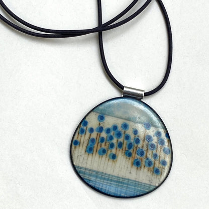 Round pendant with blue and brown pattern on a black cord against a white background