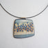 Square pendant with blue and beige pattern on a black cord against a light gray background