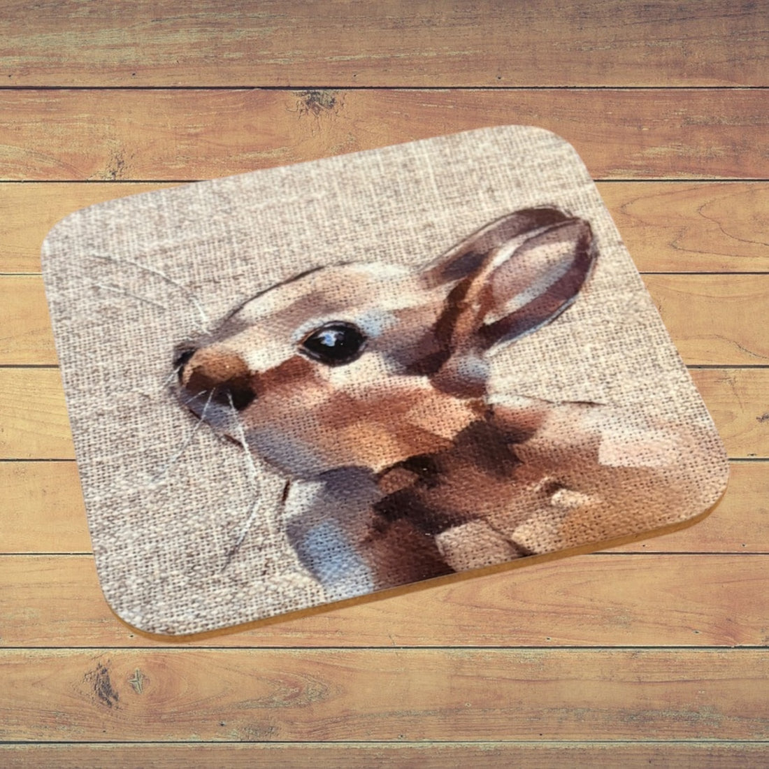 A rectangular bath mat with rounded corners featuring a printed rabbit design on a textured beige background, displayed on a wooden plank floor.