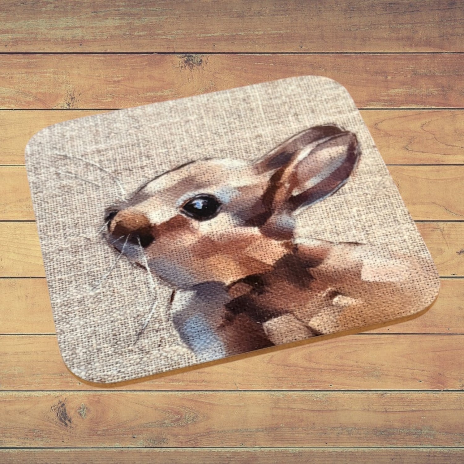 A rectangular bath mat with rounded corners featuring a printed rabbit design on a textured beige background, displayed on a wooden plank floor.