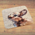 A rectangular bath mat with rounded corners featuring a printed rabbit design on a textured beige background, displayed on a wooden plank floor.