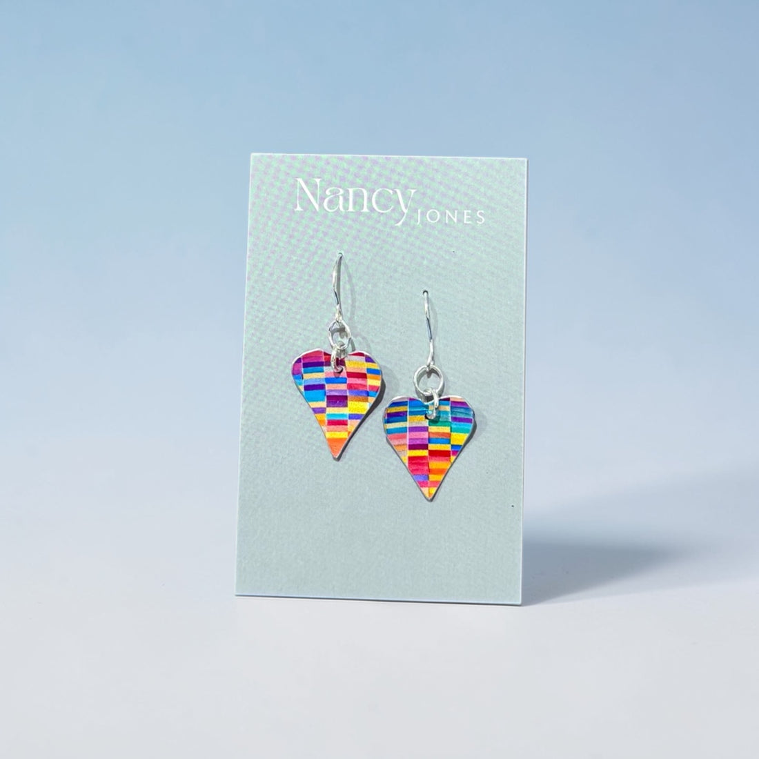 Colorful heart-shaped earrings on a Nancy Jones card against a light blue background