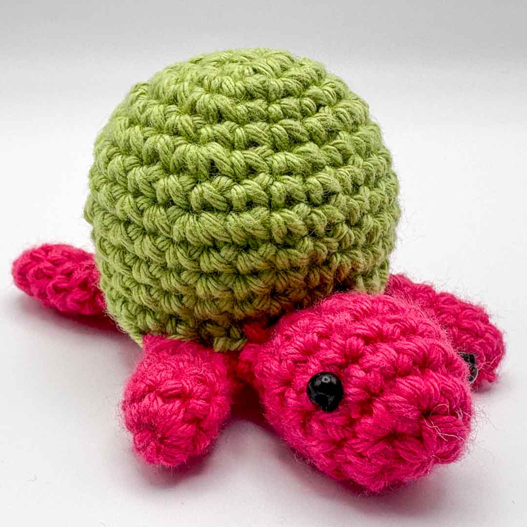 Crocheted turtle toy with green shell and pink body on a white background_Crochet Turtle - Hooked on Yarn_Just Makers