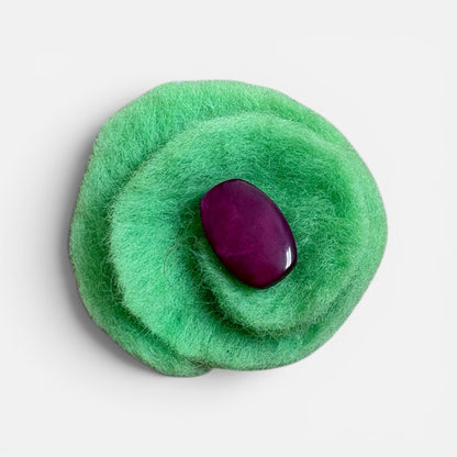 Green felt brooch with a purple stone on a light gray background