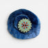Blue felted flower with a circular embroidered center on a white background