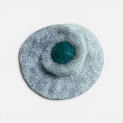 Round gray felted product with a central teal circle on a light gray background