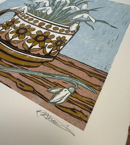 A close-up of a printed artwork showing a patterned cup filled with white snowdrops, with a signature below the print on a white paper background.