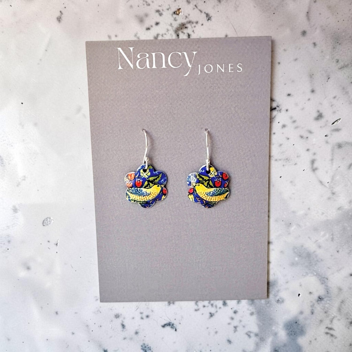 Colorful heart-shaped earrings on a Nancy Jones card against a marble background
