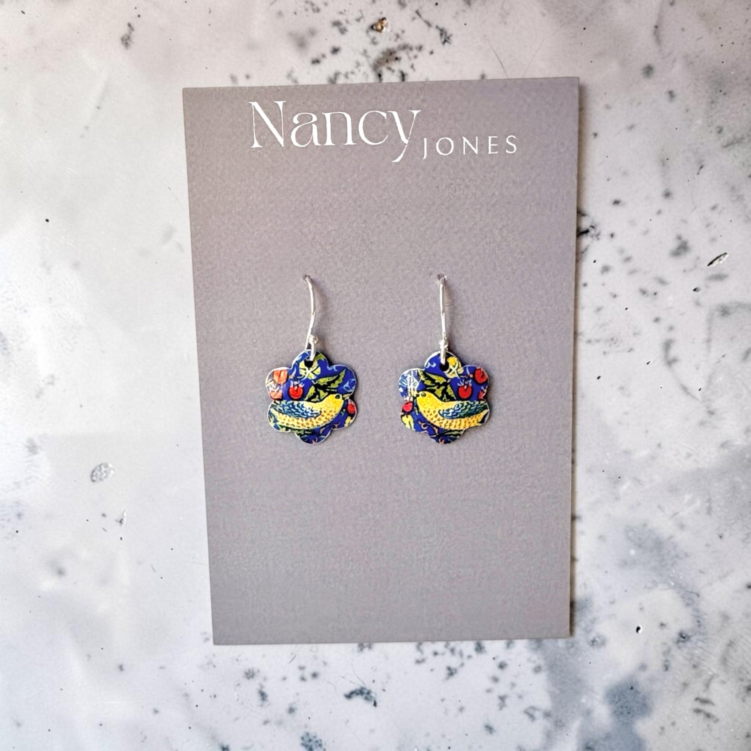 Colorful heart-shaped earrings on a Nancy Jones card against a marble background