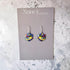 Colorful heart-shaped earrings on a Nancy Jones card against a marble background